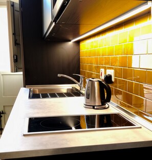 A kitchen with a stainless steel sink, a kettle, and a tiled backsplash. - Savynomad Harbour Residences Bormla (Cospicua)