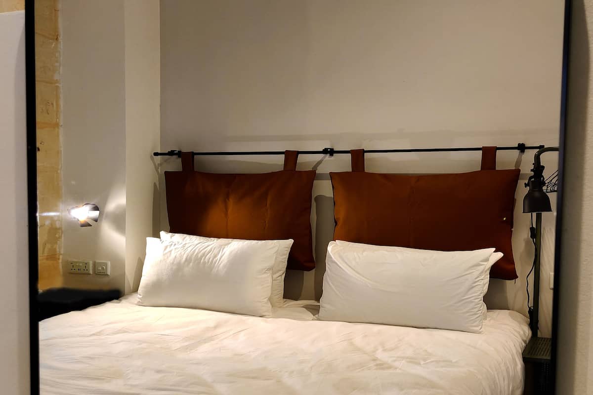 A bed with white bedding, two pillows, and a headboard with brown cushions.