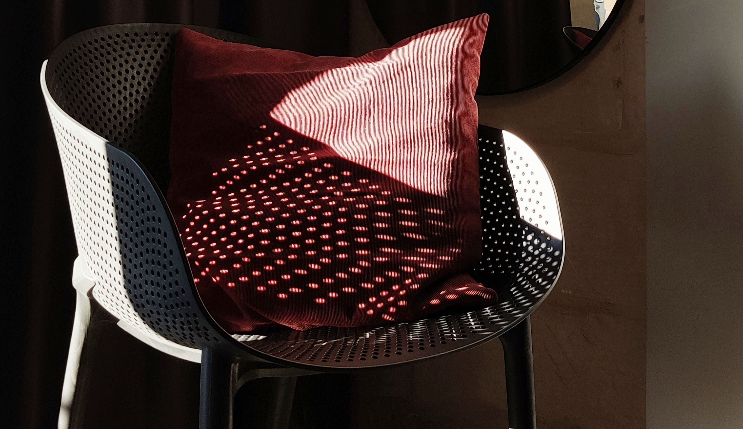 Une chaise dotée d’un coussin à motifs rouges et d’une structure en métal perforé.