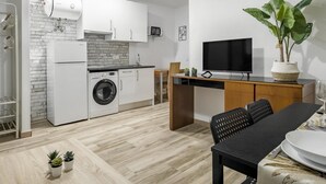 Een moderne keuken met een vaatwasser, wasmachine en een inbouwoven. Er is een eethoek met een tafel, stoelen en een televisie.