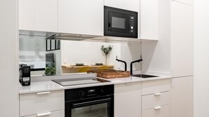 Une cuisine moderne avec des armoires blanches, un micro-ondes noir, un four encastré et un évier en acier inoxydable.