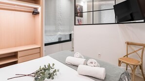 Une chambre d’hôtel moderne, équipée d’un lit, d’une armoire en bois, d’un miroir et d’une fenêtre donnant sur un paysage agréable.