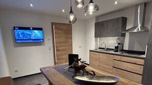 A modern kitchen with wooden cabinets, a stainless steel sink, and a built-in oven. There is a decorative deer sculpture on the dining table.