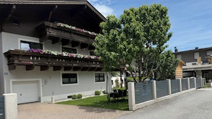 A two-story building with a balcony adorned with flowers, a covered outdoor seating area, and a paved driveway.