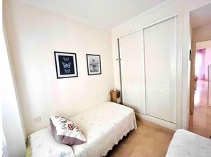 A small bedroom with a single bed, a nightstand, a wardrobe, and two framed pictures on the wall.