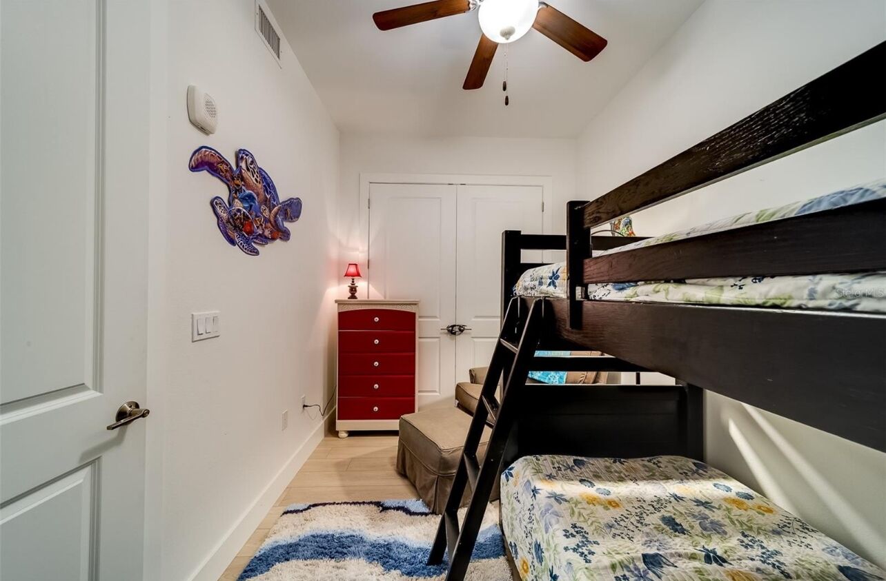 Un dormitorio con literas, un aparador rojo, un ventilador de techo y una decoración en la pared.