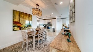 A modern kitchen with white cabinets, a dining area with a wooden table and chairs, and a large abstract painting on the wall. - Luxury new condo steps to the beach with Gulf Views, heated pool, & hot tub (Madeira Beach)