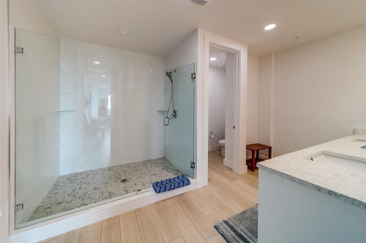 Een moderne badkamer met een douchecabine van glas, een wit wastafelmeubel en een houten vloer.