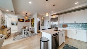 A modern kitchen with white cabinets, a stainless steel dishwasher, and pendant lighting. - Luxury new condo steps to the beach with Gulf Views, heated pool, & hot tub (Madeira Beach)