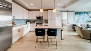 A modern kitchen with a central island, stainless steel appliances, and pendant lighting. - Luxury new condo steps to the beach with Gulf Views, heated pool, & hot tub (Madeira Beach)