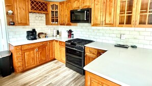 Una cocina con armarios de madera, una estufa negra, un microondas y una encimera blanca.