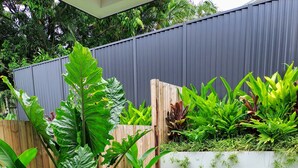 Een verzorgde tuin met verschillende planten, een houten omheining en een witte muur.