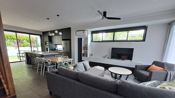Een moderne woonkamer met een grote grijze bank, een klein rond tafeltje en een aan de muur bevestigde televisie.