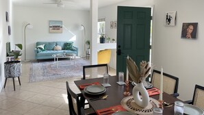 A modern living room with a blue sofa, a dining table set for four, and a green door in the background.