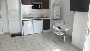 A compact kitchen with white cabinets, a microwave, a refrigerator, a dishwasher, and a small table with a chair. - Appartement T2 Tout Confort, Grand Balcon, Saint Nazaire Ouest (Saint-Nazaire)