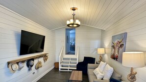 Ein modernes Wohnzimmer mit Flachbildfernseher, einer Treppe zu einer oberen Ebene, einem Couchtisch, einer Couch und einer Lampe.
