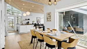 Una cucina moderna con mobili bianchi, un'area pranzo con tavolo e sedie in legno e un'ampia finestra che si affaccia su un giardino.