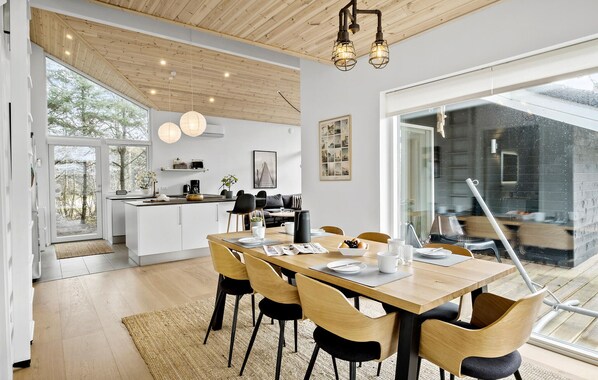 A modern kitchen with white cabinets, a dining area with a wooden table and chairs, and a large window overlooking a garden.