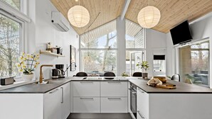 Una cucina moderna con mobili bianchi, un'isola centrale, illuminazione a sospensione e ampie finestre con vista sull'esterno.