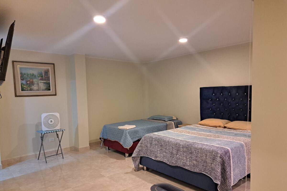 A bedroom with two beds, a standing fan, and a framed picture on the wall.