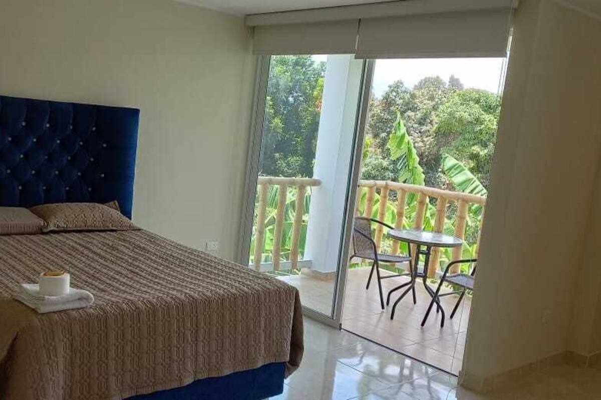 A bedroom with a large bed, a nightstand, and a balcony with a table and chairs.