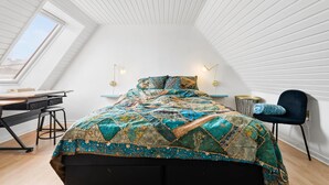 Una camera da letto con soffitto spiovente, un letto con copripiumino a fantasia, una scrivania e una sedia.