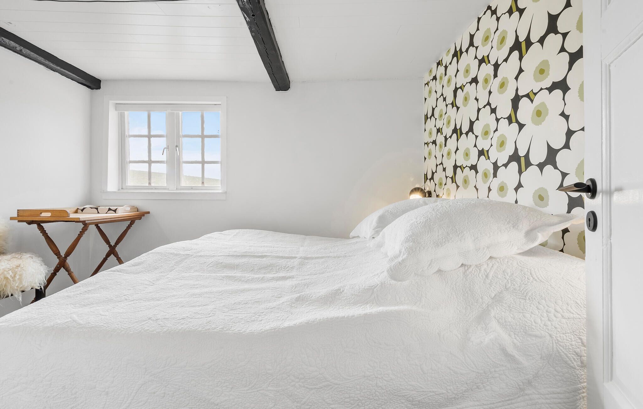 Une chambre avec un grand lit, une petite table en bois, un oreiller blanc moelleux et une fenêtre aux cadres blancs.