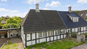 Una casa tradizionale con struttura a telaio in legno e intonaco, un tetto ripido, un camino e un piccolo giardino con vialetto in ghiaia e recinzione in legno.
