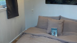 Et soveværelse med seng, et maleri, et vindue med gardiner og en vægmonteret lampe.
