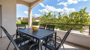 Ein Balkon mit Tisch und Stühlen, eine Banane auf dem Tisch und Blick auf Grünflächen und Gebäude.