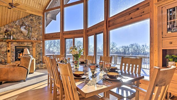Une table à manger en bois, assortie à des chaises, une cheminée en pierre et une grande fenêtre donnant sur un paysage enneigé.