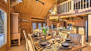 L’intérieur d’un chalet en bois comprend une salle à manger avec une table dressée pour six personnes, un coin cuisine et une mezzanine ornée d’une tête de cerf fixée au mur.