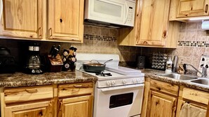 A kitchen with wooden cabinets, a stove, a microwave, and a granite countertop.