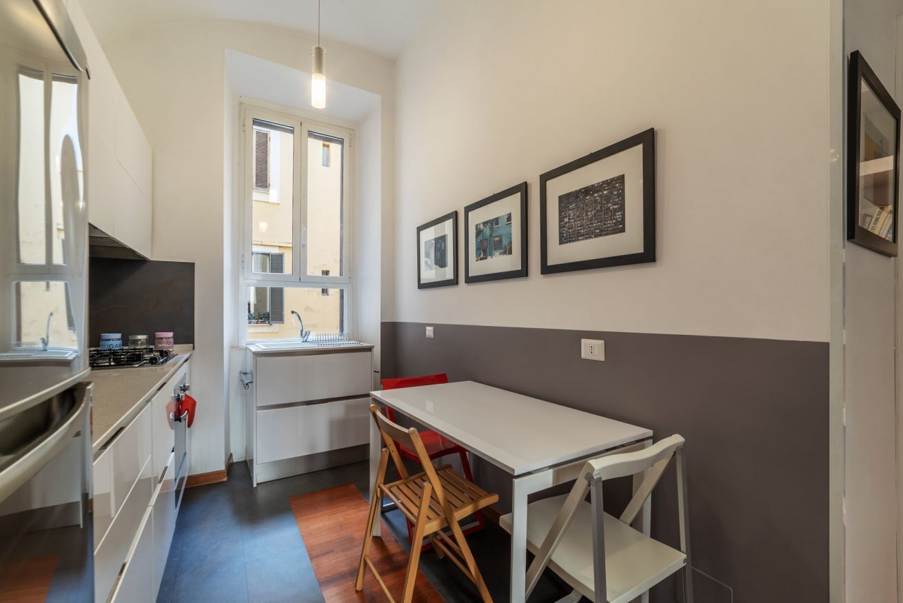A compact kitchen with a dining area, a window, and framed pictures on the wall.