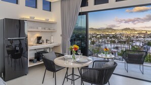 A modern kitchen with a refrigerator, dining table, and chairs. A large window offers a city view.
