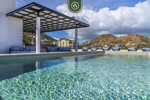 Zona de piscina con área de descanso cubierta y montañas al fondo.