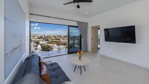 A modern living room with a large window, a ceiling fan, a flat-screen TV, a sofa, and a small round table with flowers.