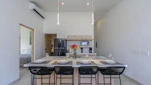 A modern kitchen with a central island, overhead lighting, and a dining area with four chairs.