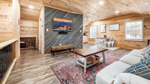 Interior acogedor de una cabaña con detalles de madera, chimenea, zona de comedor y un ventanal grande.
