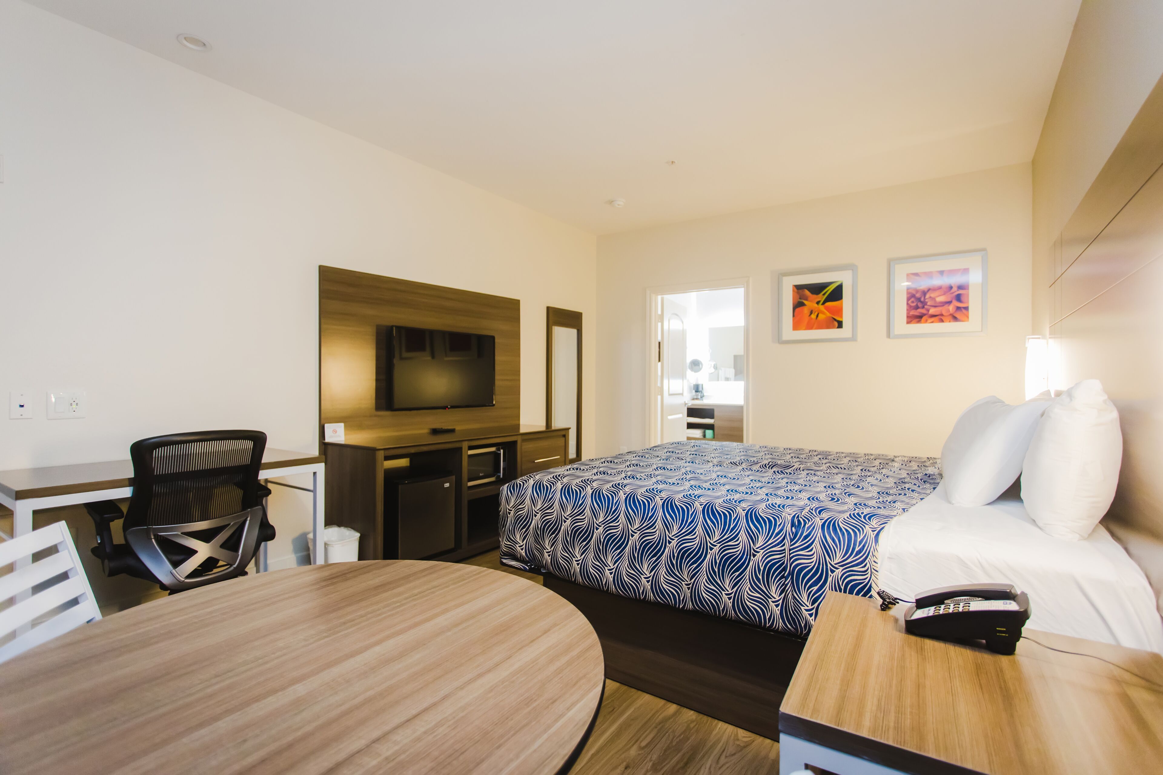 A hotel room with a bed, a desk, a chair, a TV, and a phone on the bedside table.