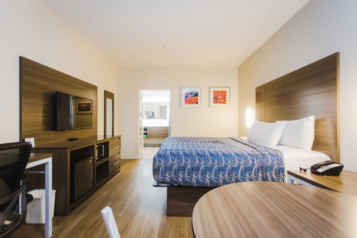 A modern hotel room with a bed, a desk, a chair, a television, and artwork on the walls.