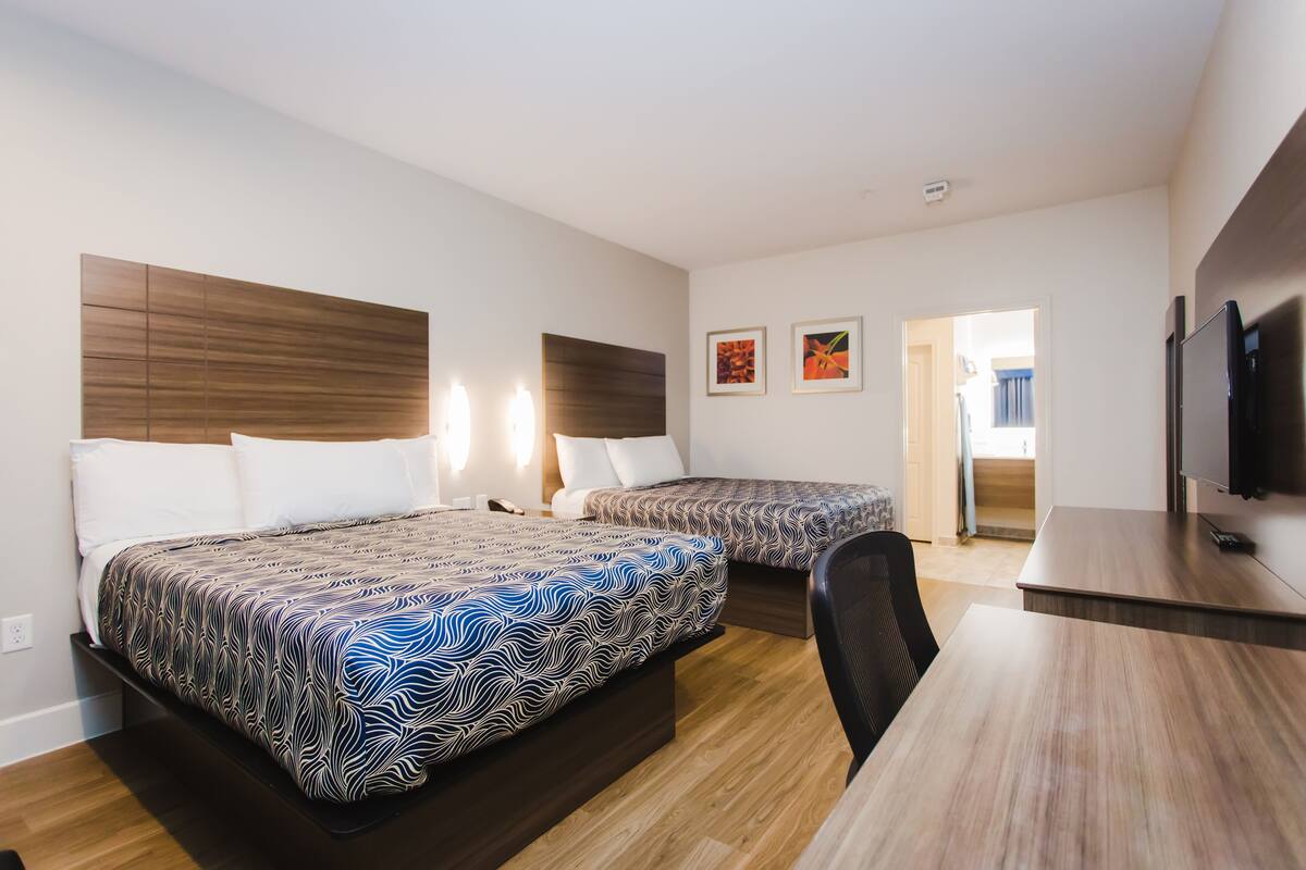 A hotel room with two beds, a desk, and a TV.