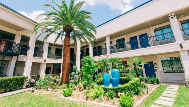 A multi-story building with a central courtyard featuring palm trees, a garden with various plants, and a blue door.