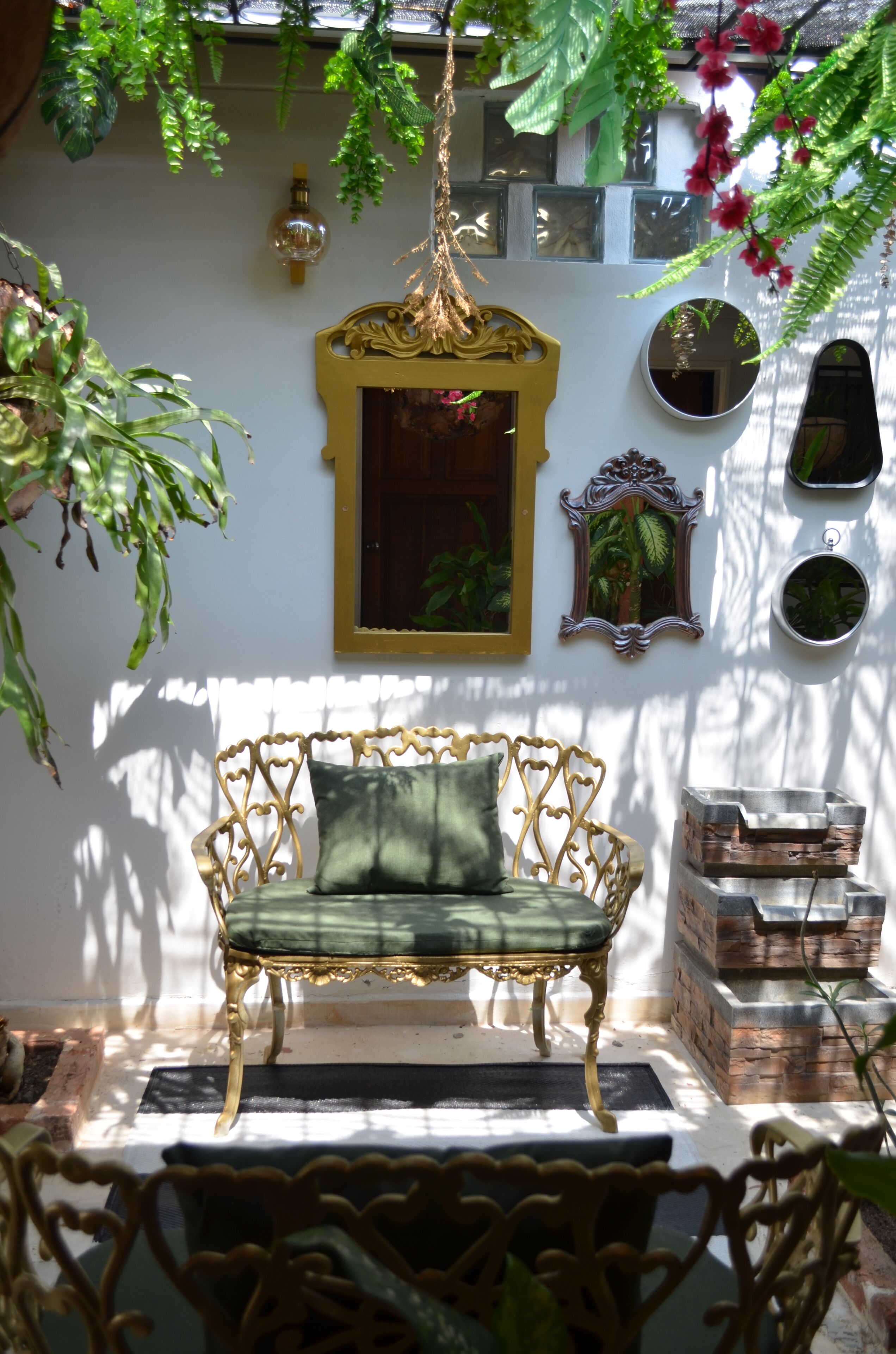 Une pièce baignée de lumière naturelle, avec un banc vert rembourré, des œuvres d’art décoratives au mur et des plantes suspendues.