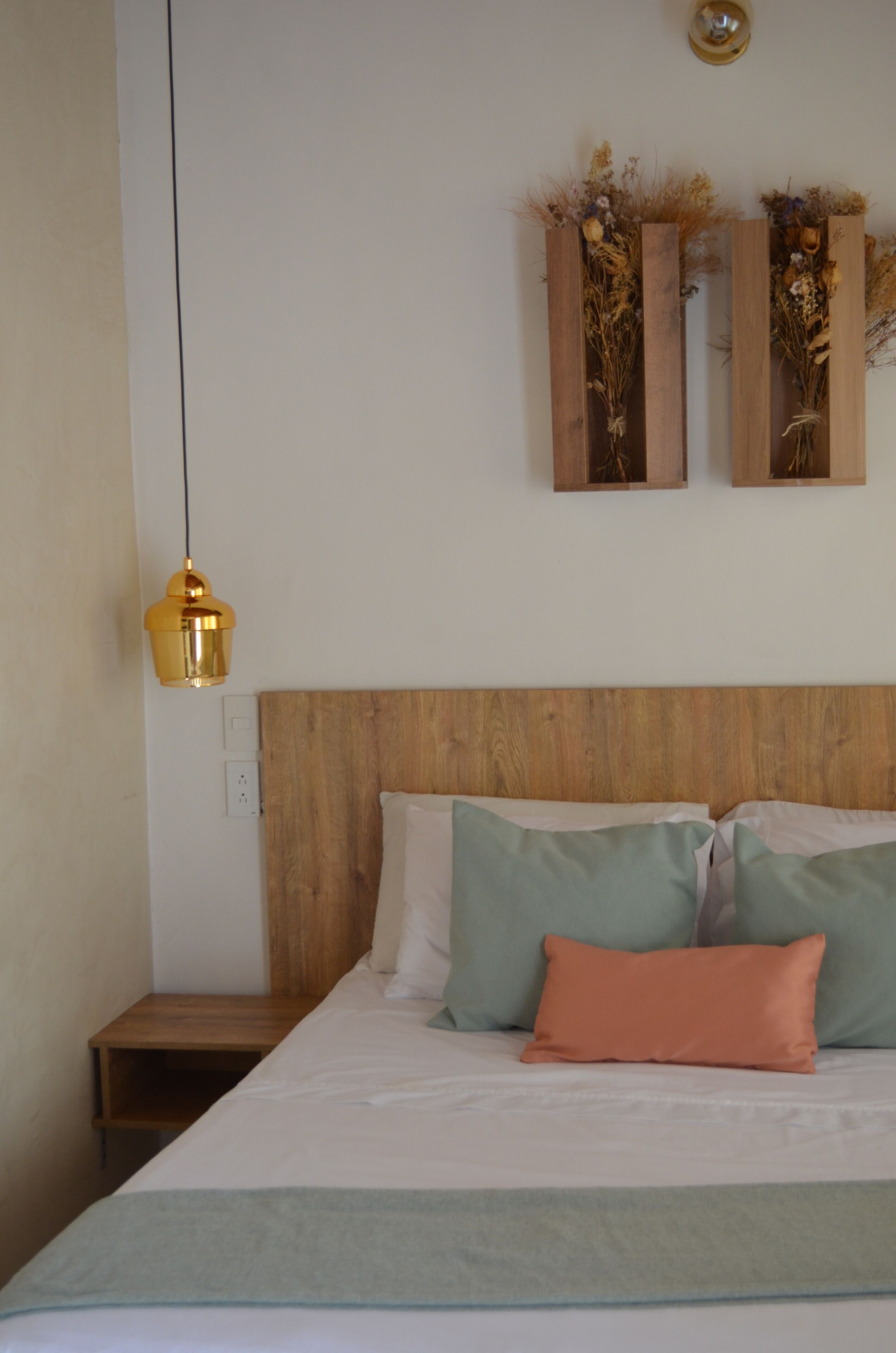 A bedroom with a wooden headboard, a bed with multiple pillows, a nightstand, and a wall-mounted light fixture.
