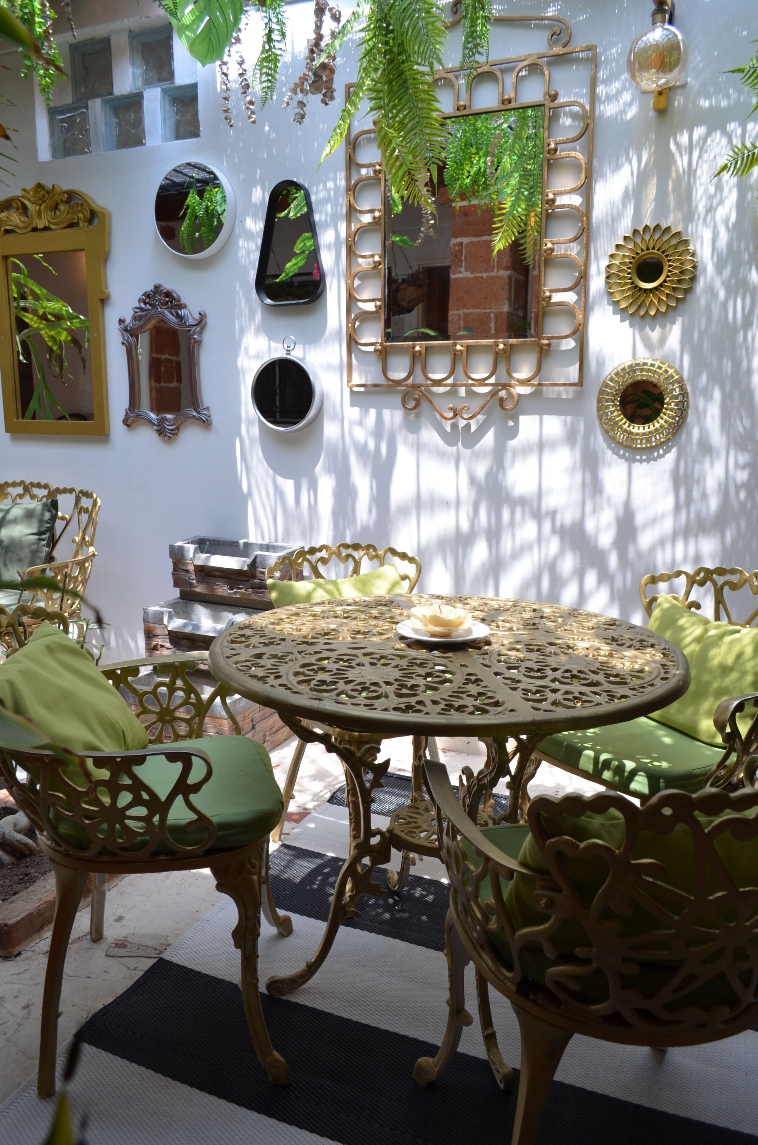 A sunlit patio with ornate metal furniture, a round table, and decorative mirrors and plants.