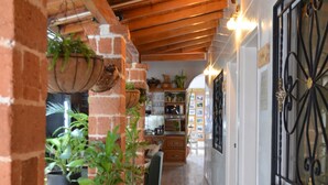 A corridor with brick walls, wooden ceiling beams, tiled flooring, and hanging planters with green plants. - Selva Maria Hotel Boutique (Santa Fe de Antioquia)