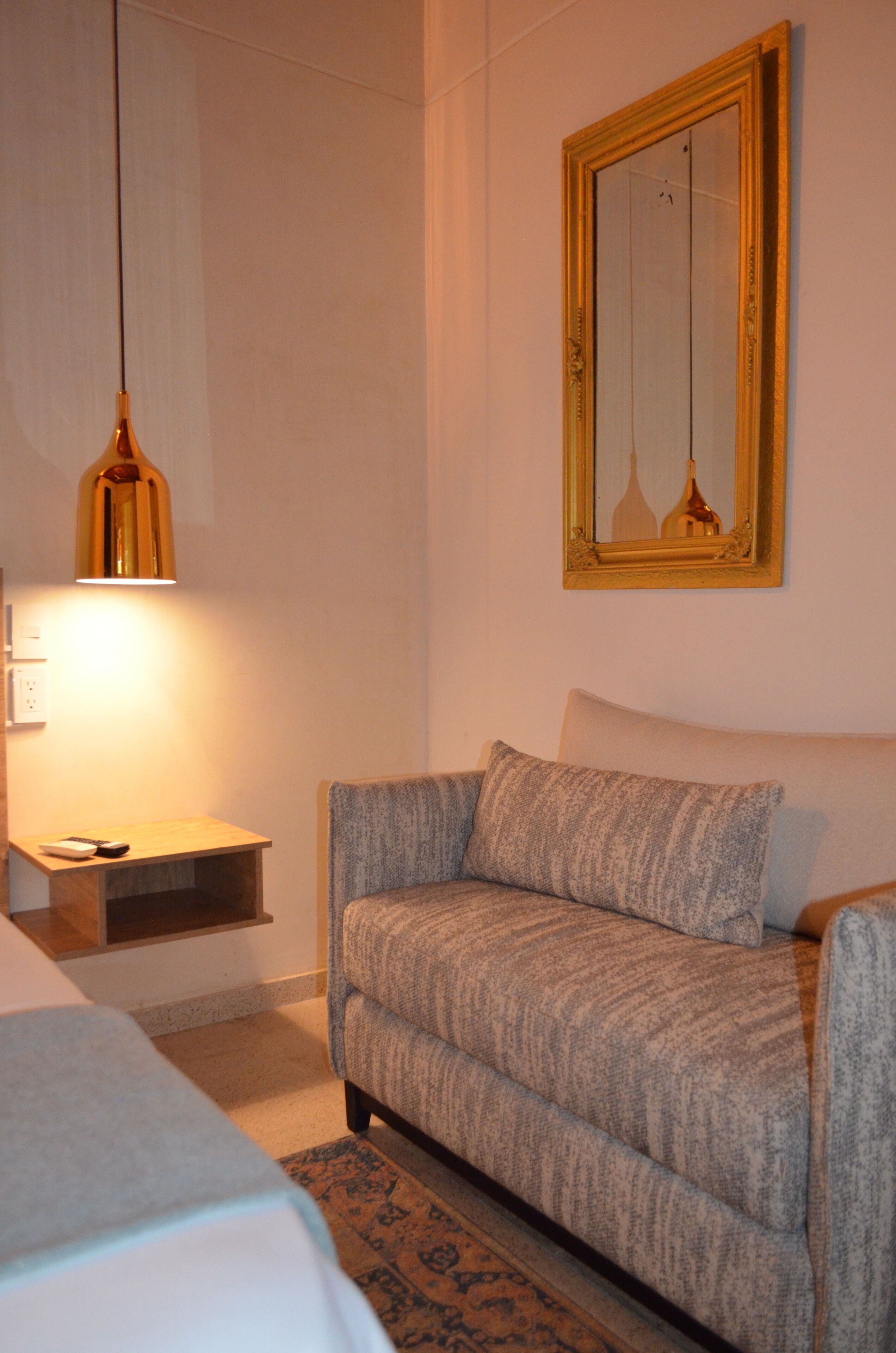 A room with a sofa, a small table with a lamp, and a mirror on the wall.