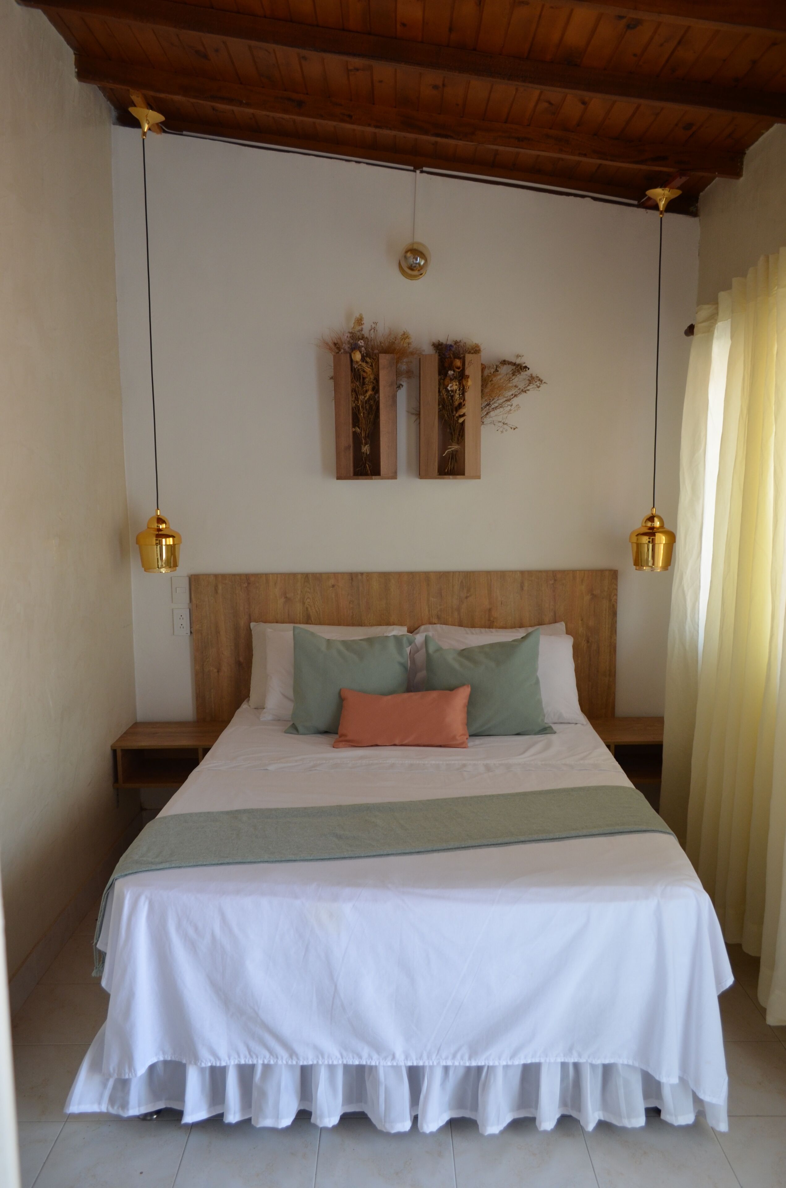 Una cama bien hecha con colcha blanca y verde, dos mesitas de noche y un cabecero de madera.