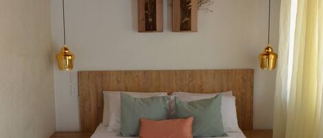 Una cama bien hecha con colcha blanca y verde, dos mesitas de noche y un cabecero de madera.